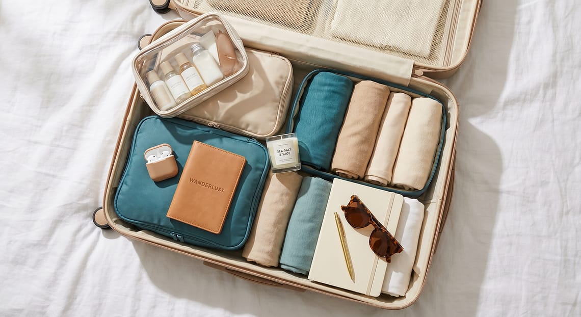 Aesthetic carry-on suitcase flatlay with travel essentials passport and journal on white bed