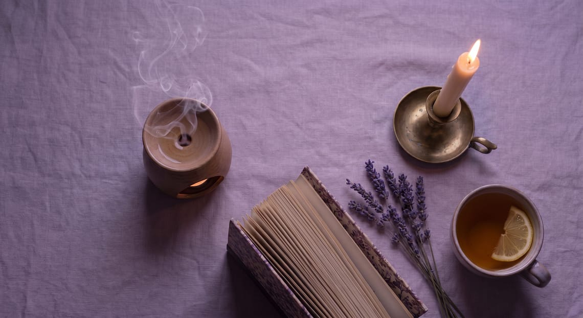 Peaceful slow living flatlay with lavender candle herbal tea and open book on linen