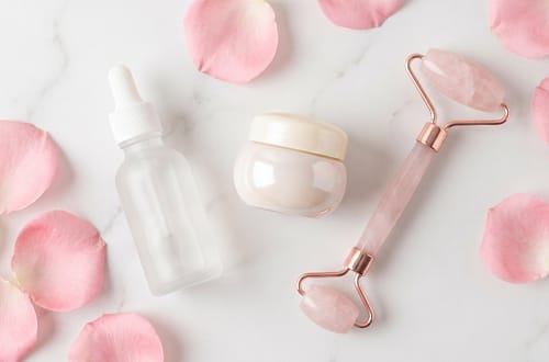 Clean beauty skincare flatlay with glass bottles and rose petals on marble