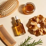 Hair care flatlay with wooden brush argan oil silk scrunchie and rosemary on cream background